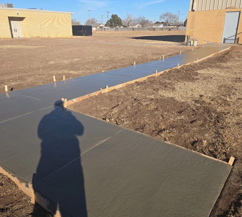 Long new sidewalk run, freshly finished in its forms, between two buildings in Lubbock