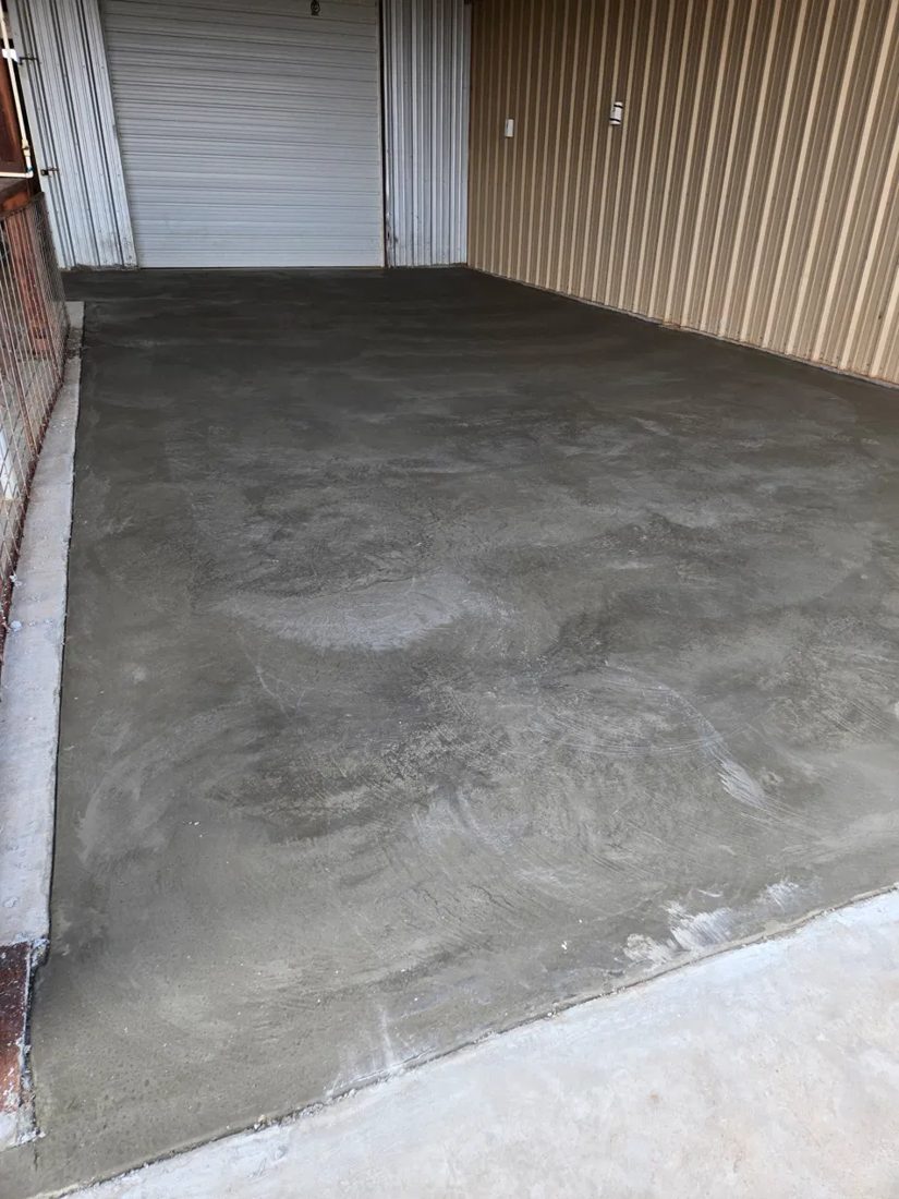 Freshly troweled concrete floor inside a metal building with a roll-up door