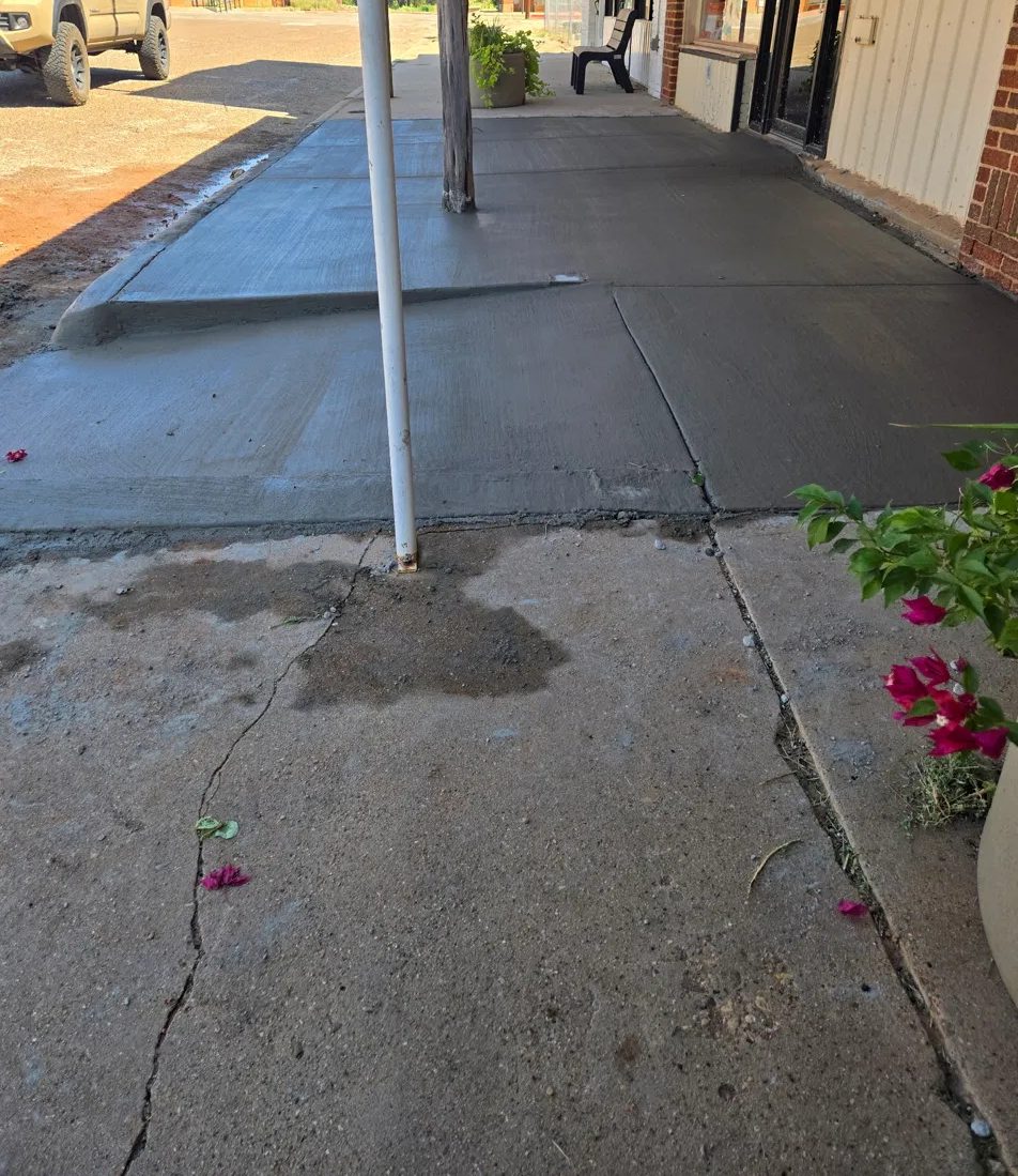 New sidewalk section poured in front of a downtown storefront, meeting the older walk